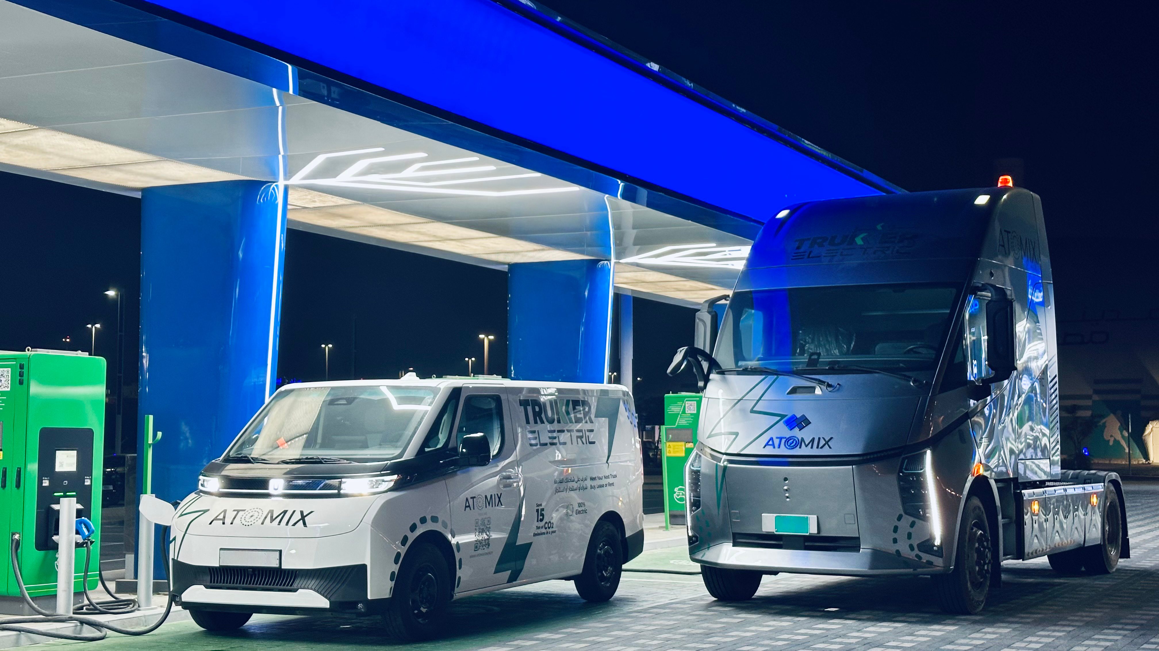 TruKKer Electric and ATOMIX electric trucks charging at a TruKKer charging station at night
